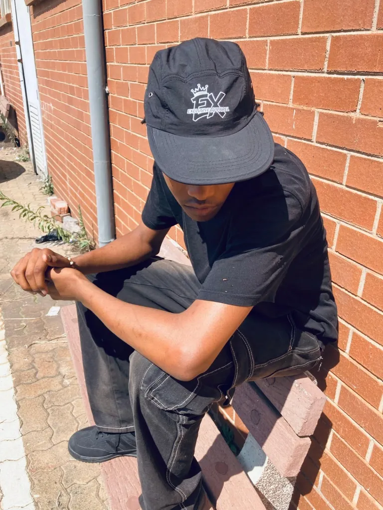 Close-up of the Exclusive Apparel crown logo on a black cap worn with a black T-shirt