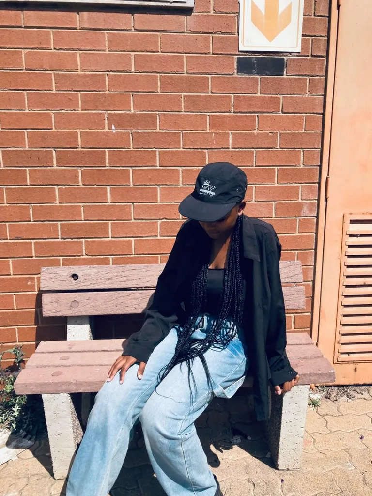 Black Exclusive Apparel cap styled with a black shirt and light denim beside a brick wall